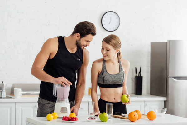 happy man preparing smoothie near sportive girl and fruits 