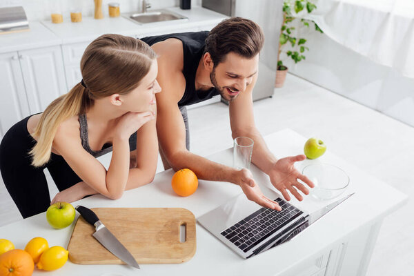 overhead view of happy man gesturing near laptop and sportive girl 