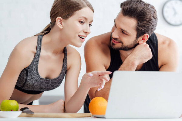 sportive girl pointing with finger at laptop near happy man 