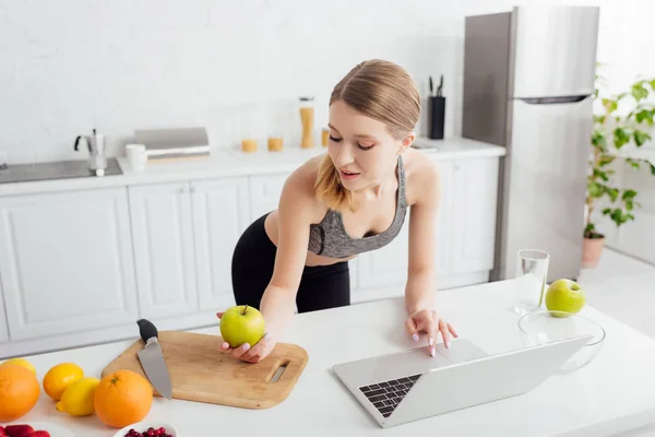 Mulher Feliz Esportiva Olhando Para Maçã Saborosa Perto Laptop — Fotografia de Stock