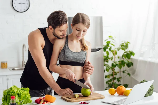 Çekici Kız Mutfaktaki Spor Adamın Yanında Elma Laptop Meyveleri Kesiyor — Stok fotoğraf