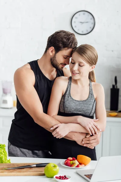 Hombre Guapo Abrazando Chica Ropa Deportiva Cerca Computadora Portátil Frutas —  Fotos de Stock