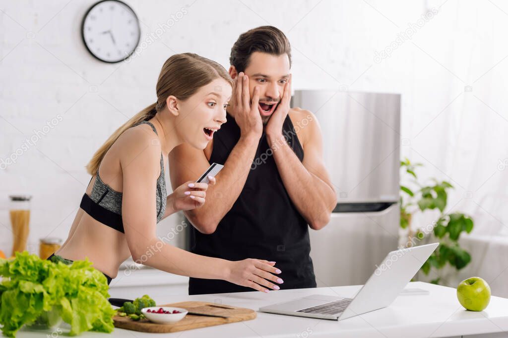 surprised man and woman looking at laptop while online shopping in kitchen 
