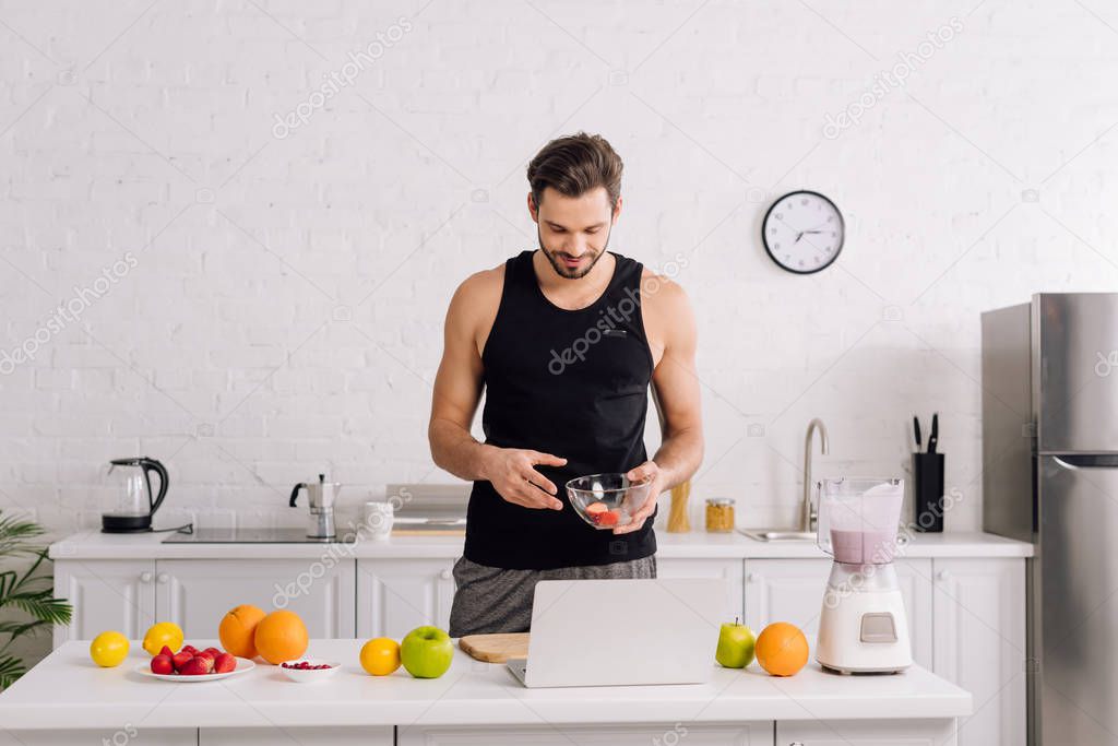 handsome man looking at laptop near tasty fruits and blender with smoothie 
