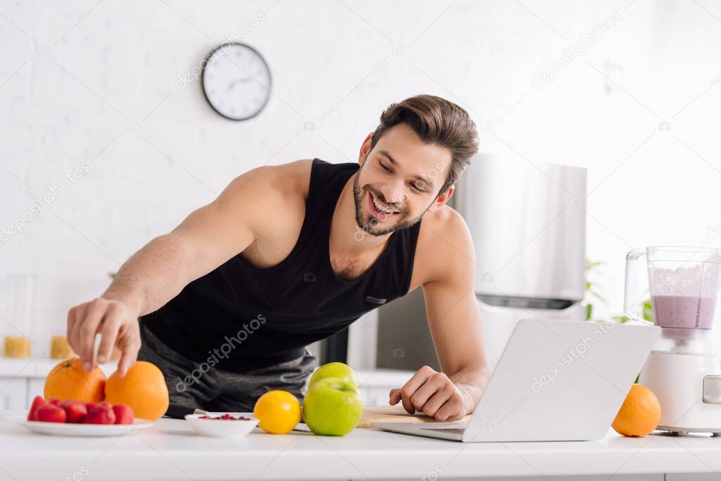 happy man near laptop, blender with smoothie and tasty fruits 