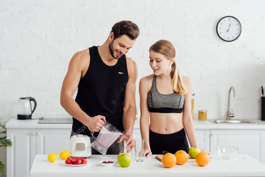 sportive man holding blender with smoothie near happy girl and fruits 