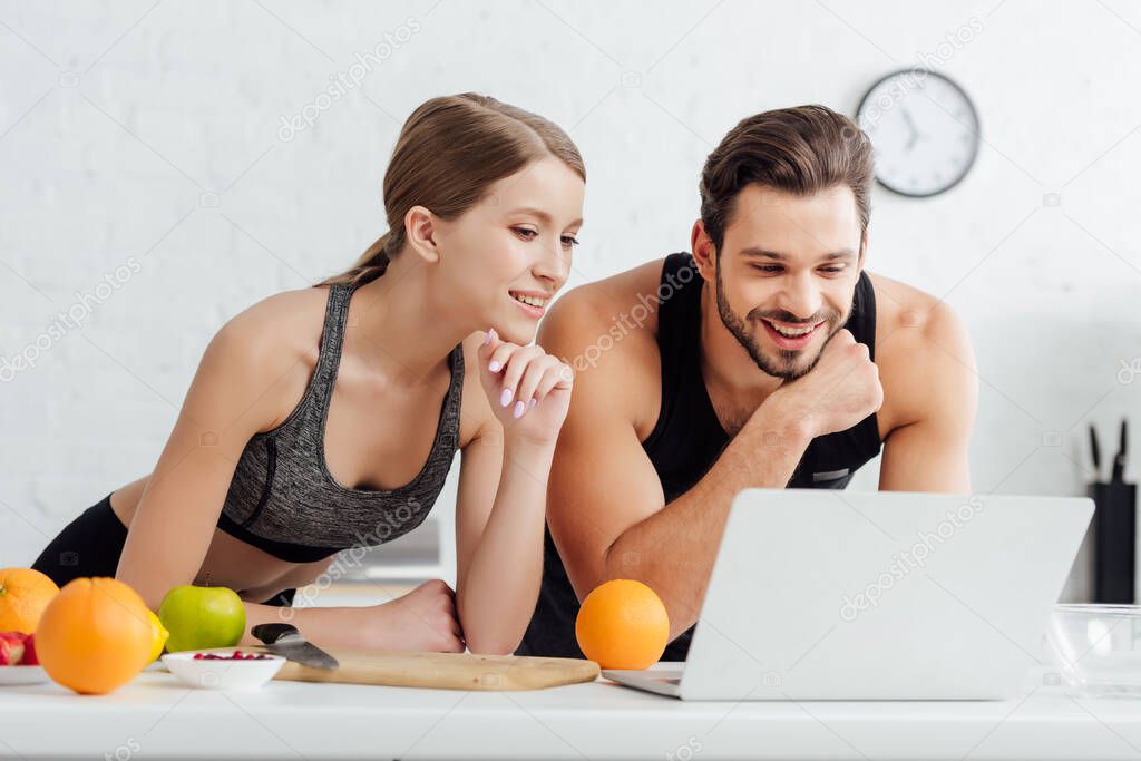 happy man and woman looking at laptop near tasty fruits 