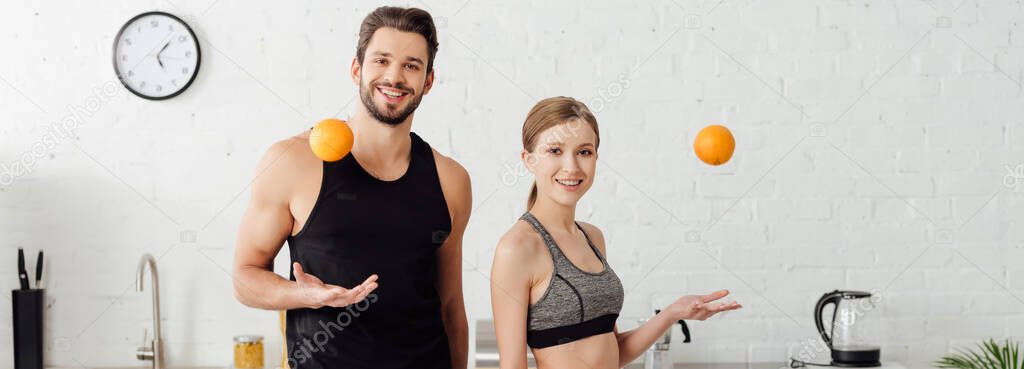 panoramic shot of sportive girl and cheerful man throwing in air oranges 