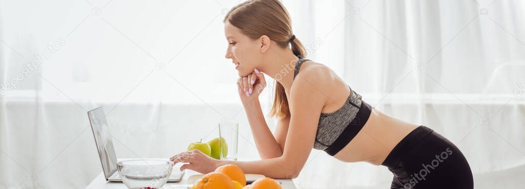 panoramic shot of happy woman in sportswear using laptop at home