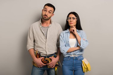 Gri üzerine alet kemeri takmış, gözlüklü düşünceli el işçileri. 