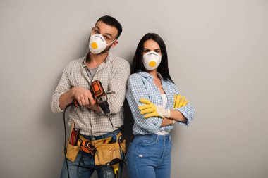 Gri üzerine elektrikli matkap tutan güvenlik maskeli kendinden emin el işçileri 