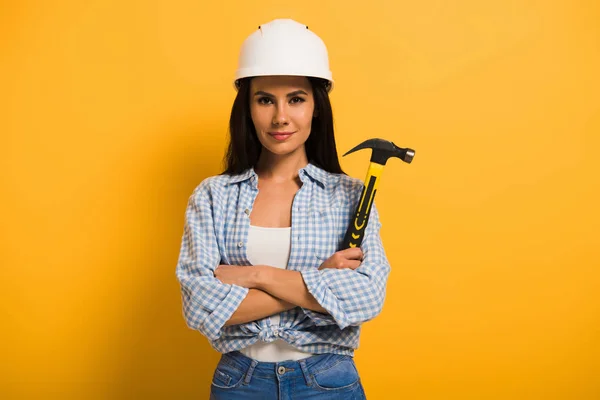 头戴头盔的有自信的女体力劳动者 手持铁锤 双手交叉 呈黄色 — 图库照片