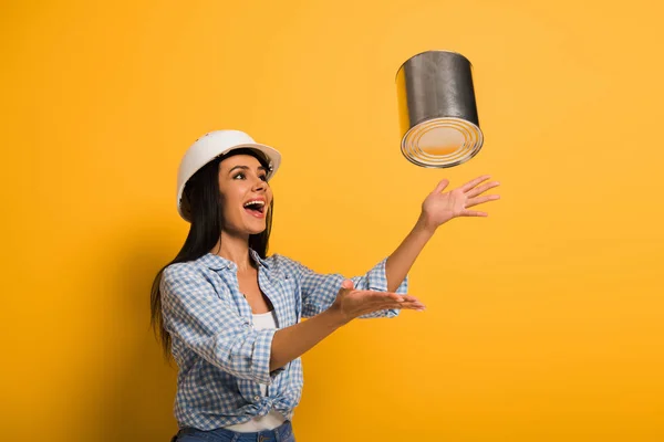 头戴安全帽的兴奋女工把油漆倒在黄色的罐子上 — 图库照片
