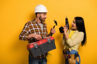 happy manual workers holding toolbox and electric drill on yellow    clipart