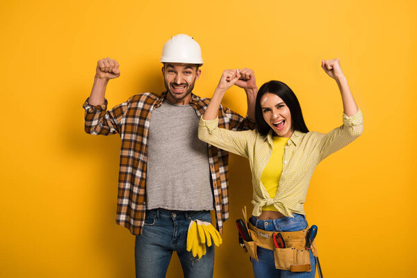 successful manual workers with hands up on yellow  