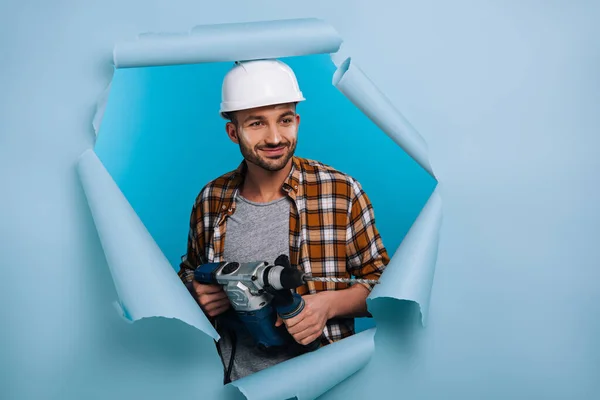 Sorrindo Reparador Capacete Segurando Broca Elétrica Papel Rasgado Isolado Azul — Fotografia de Stock