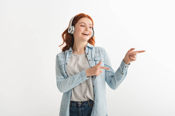 excited teen girl listening music with headphones and pointing isolated on white