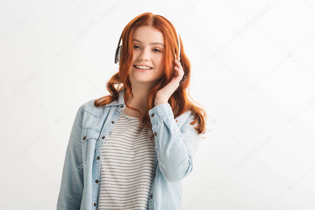 cheerful attractive redhead teen girl listening music with headphones, isolated on white