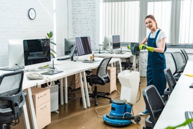 neşeli temizlikçi temizlik makinesiyle yerleri yıkarken kameraya bakıyor.