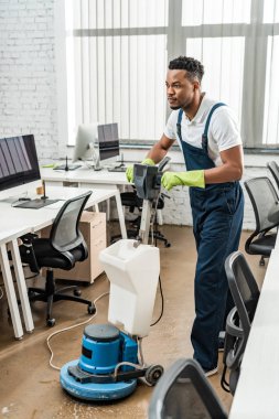 Yakışıklı Afro-Amerikan temizleyici ofiste temizlik makinesiyle yerleri yıkıyor.