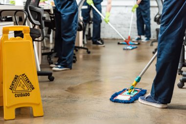 cropped view of team of young cleaners washing floor with mops in office clipart