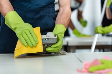 partial view of cleaner in rubber gloves cleaning office phone with rag clipart