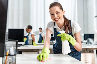 selective focus of smiling cleaner washing office desk with rag clipart