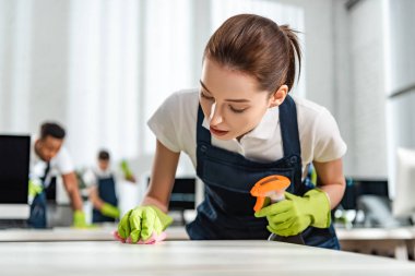 attentive cleaner in uniform cleaning office desk with rag clipart