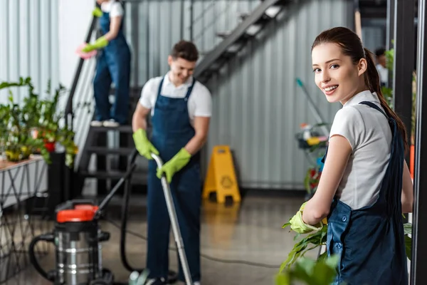 Atractivo Limpiador Sonriendo Cámara Mientras Colegas Limpieza Oficina —  Fotos de Stock