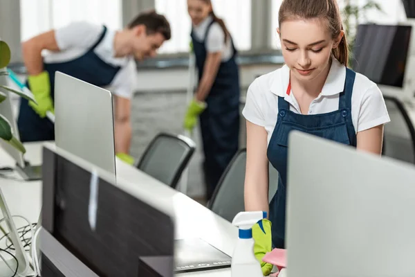 Selective Focus Pretty Cleaner Wiping Desk While Colleagues Cleaning Floor — Stock Photo, Image