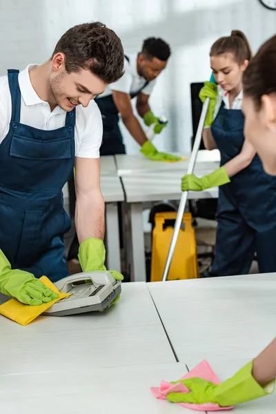 Junge Reinigungskräfte Wischen Telefon Und Schreibtisch Neben Multikulturellen Kollegen — Stockfoto