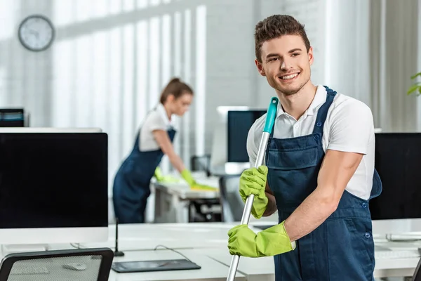 Lächelnd Sauberer Waschboden Während Kollege Schreibtisch Putzt — Stockfoto