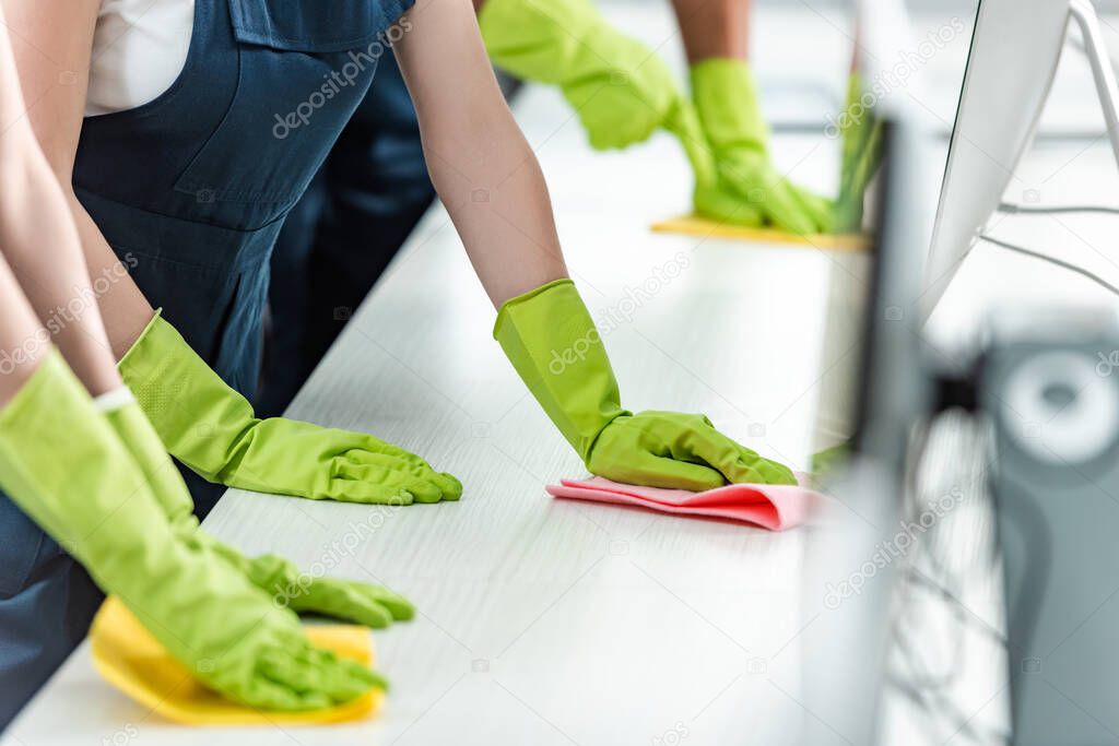 cropped view of cleaners in rubber gloves cleaning office desk 