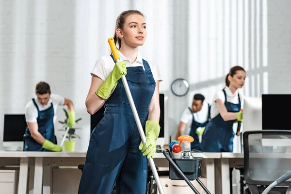 Nachdenkliche Putzfrau Hält Wischmopp Der Hand Und Schaut Bei Multikulturellen — Stockfoto