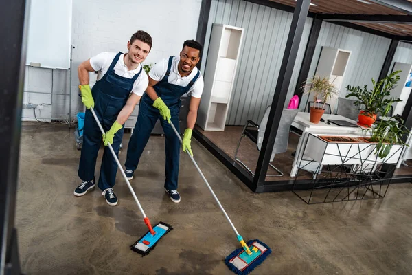 Dos Limpiadores Multiculturales Sonrientes Lavando Piso Con Trapeadores Mirando Cámara — Foto de Stock