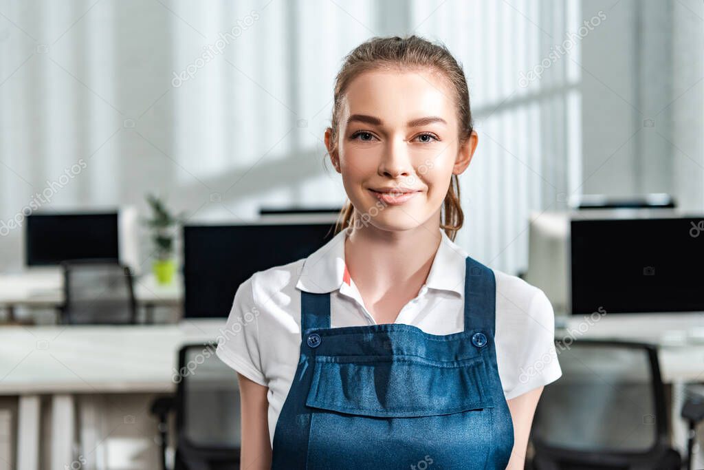attractive young cleaner in overalls smiling at camera
