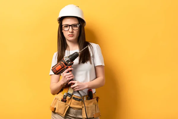 Ernstige Klusjesvrouw Houden Boor Kijken Naar Camera Gele Achtergrond — Stockfoto