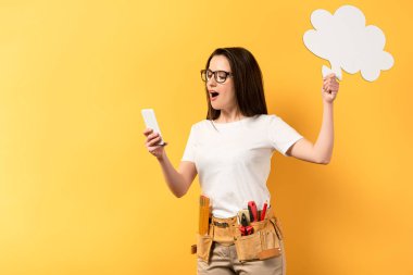 Şok olmuş tamirci kadın düşünce baloncuğu tutuyor ve sarı arka planda akıllı telefon kullanıyor. 
