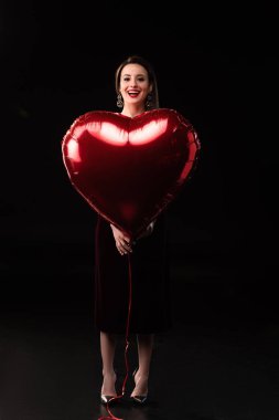 Gülümseyen kadın siyah arka planda kalp şeklinde balon tutuyor. 