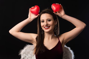 Gülümseyen kadın kanatlı, kalp şeklinde mankenler taşıyan siyah elbiseli.