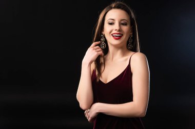 Küpeli, gülümseyen bir kadın siyah arka plana bakıyor. 