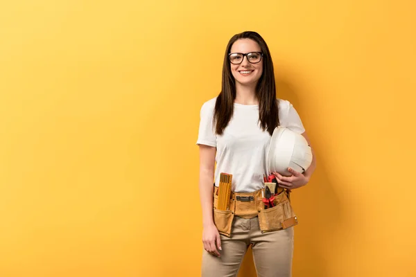 Smiling Handywoman Holding Helmet Looking Camera Yellow Background — Stock Photo, Image