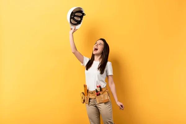 Surprised Handywoman Holding Looking Helmet Yellow Background — Stock Photo, Image