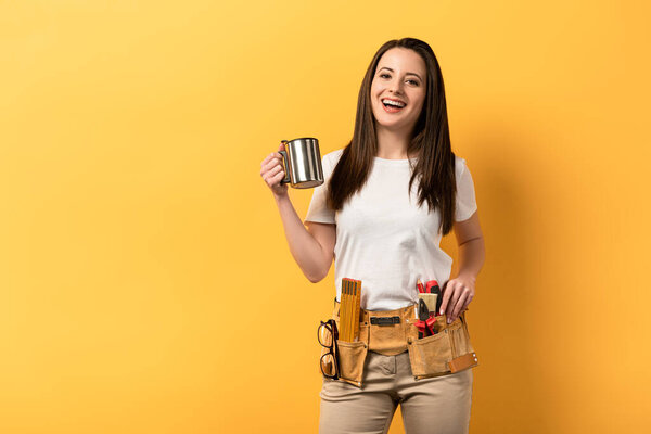 smiling handywoman holding metal cup on yellow background 