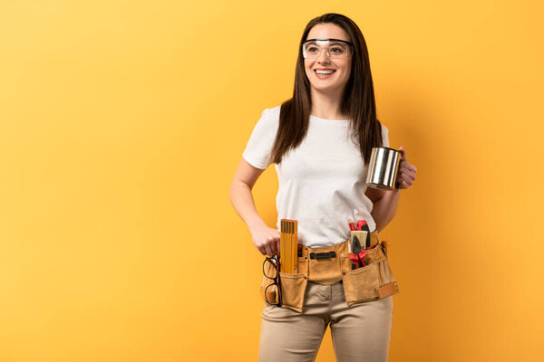 smiling handywoman holding metal cup on yellow background 