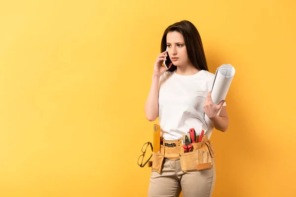 Serious Handywoman Talking Smartphone Holding Project Yellow Background — Stock Photo, Image