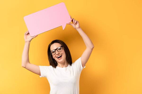 smiling woman holding speech bubble with copy space on yellow background 