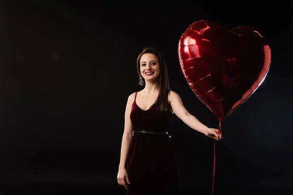 Χαμογελαστή Γυναίκα Φόρεμα Κρατώντας Μπαλόνι Σχήμα Καρδιάς Απομονωμένο Μαύρο — Φωτογραφία Αρχείου
