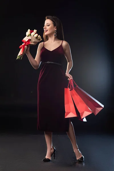 Lächelnde Frau Kleid Mit Einkaufstaschen Und Blumenstrauß Auf Schwarzem Hintergrund — Stockfoto