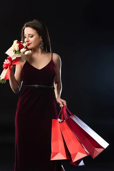 Smiling Woman Dress Holding Shopping Bags Smelling Bouquet Black Background — Stock Photo, Image
